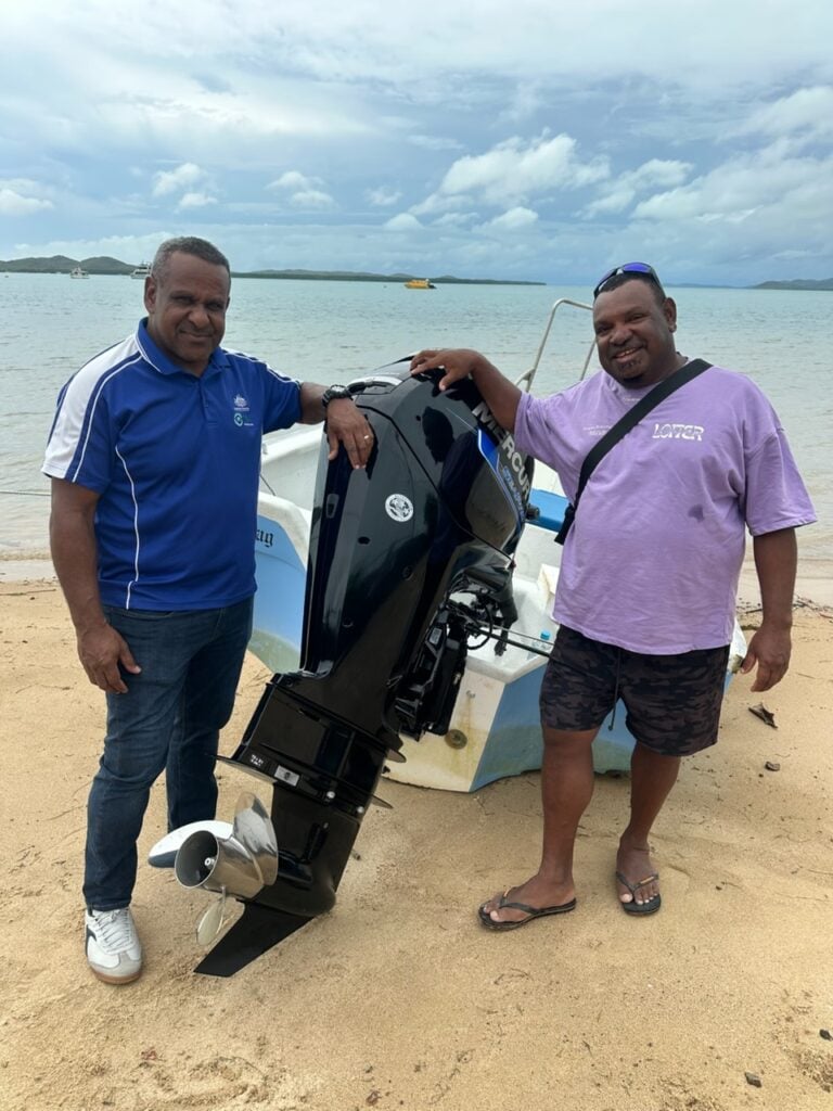 TSRA Chairperson George Nona with David Baragud and his new outboard motor on the beach near Thursday Island with sea in background.