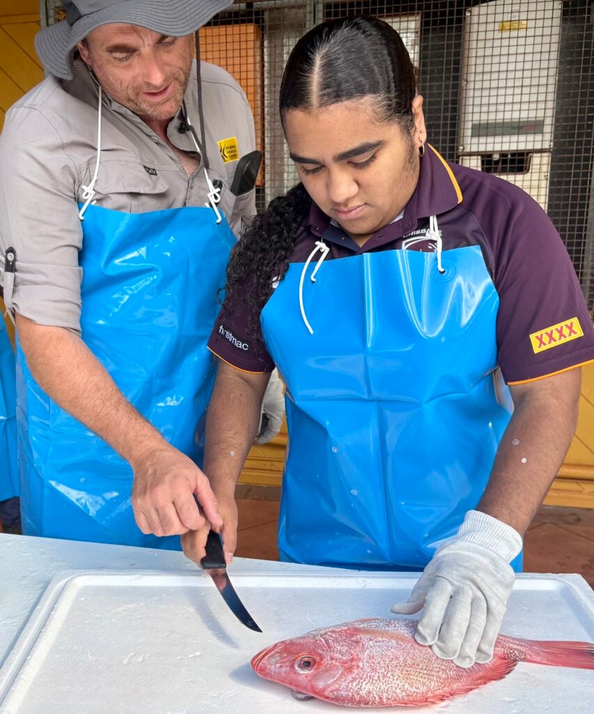 Close up of a man showing a young Torres Strait Islander woman how to fillet a fish as part of a seafood processing course in Bamaga.
