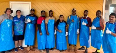A group of Torres Strait Islanders in aprons smiling with thumbs up after completing a seafood processing course in Bamaga, Torres Strait region.