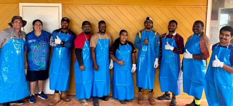 A group of Torres Strait Islanders in aprons smiling with thumbs up after completing a seafood processing course in Bamaga, Torres Strait region.