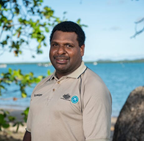 A smiling Torres Strait Islander man in ranger uniform infront of ocean of the Torres Strait region.